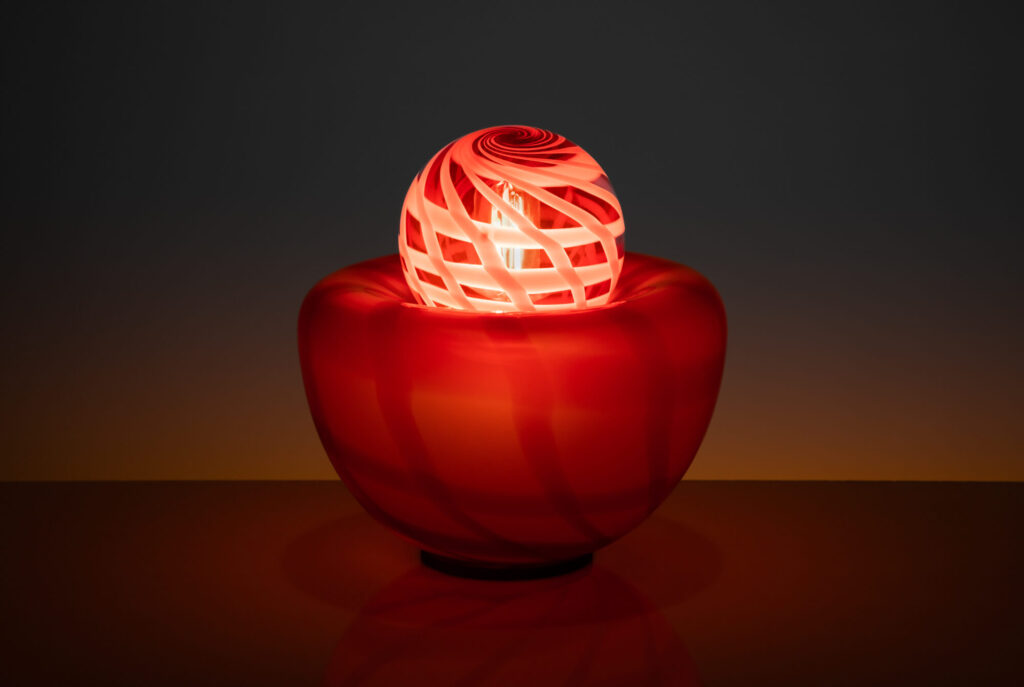 Lampe de table rose quadrillé, en verre soufflé artisanale sur un fond foncé, vue de face.