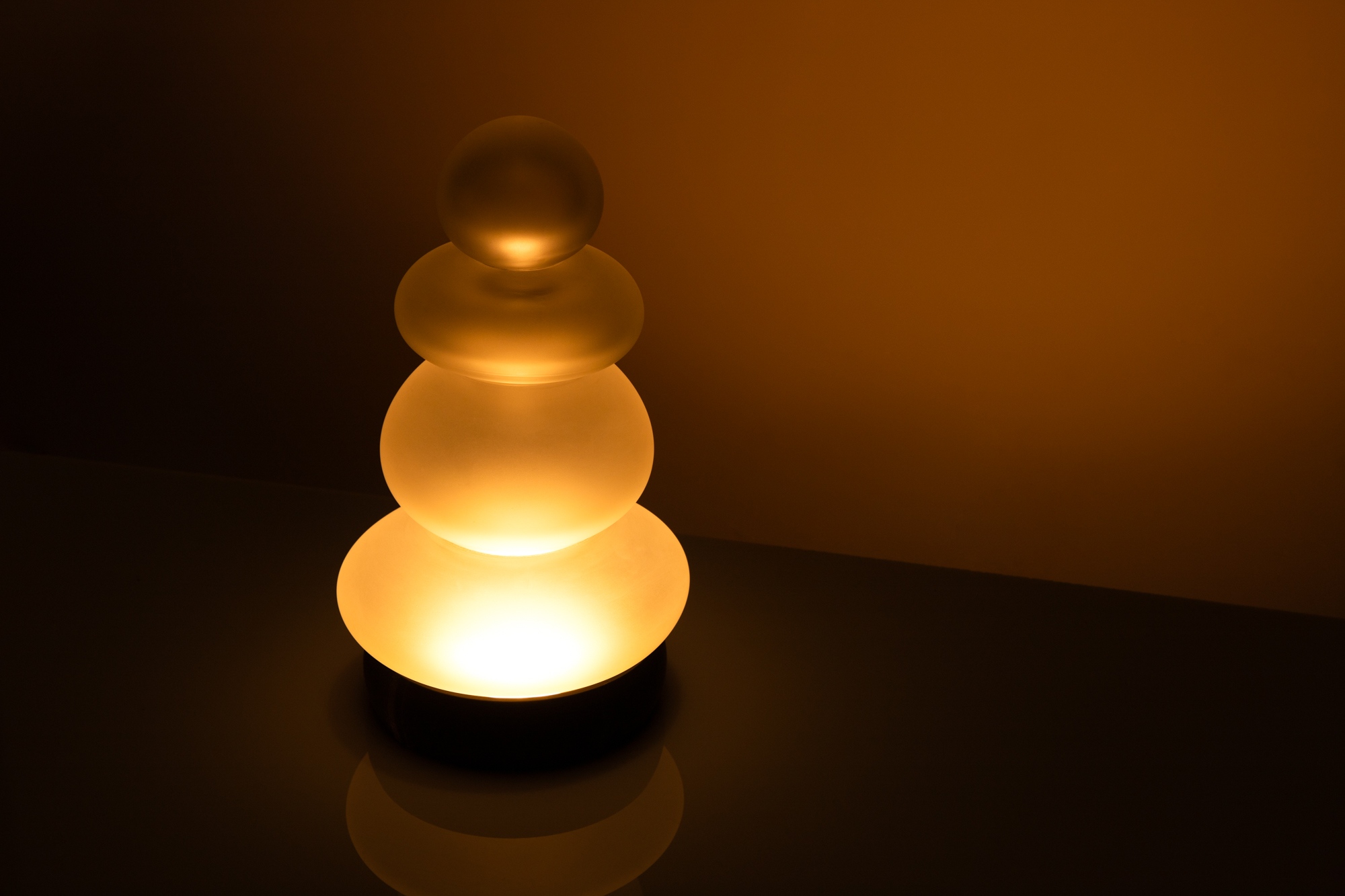 Lampe de table en verre soufflé transparent artisanale sur un fond ambre, vue de côté.