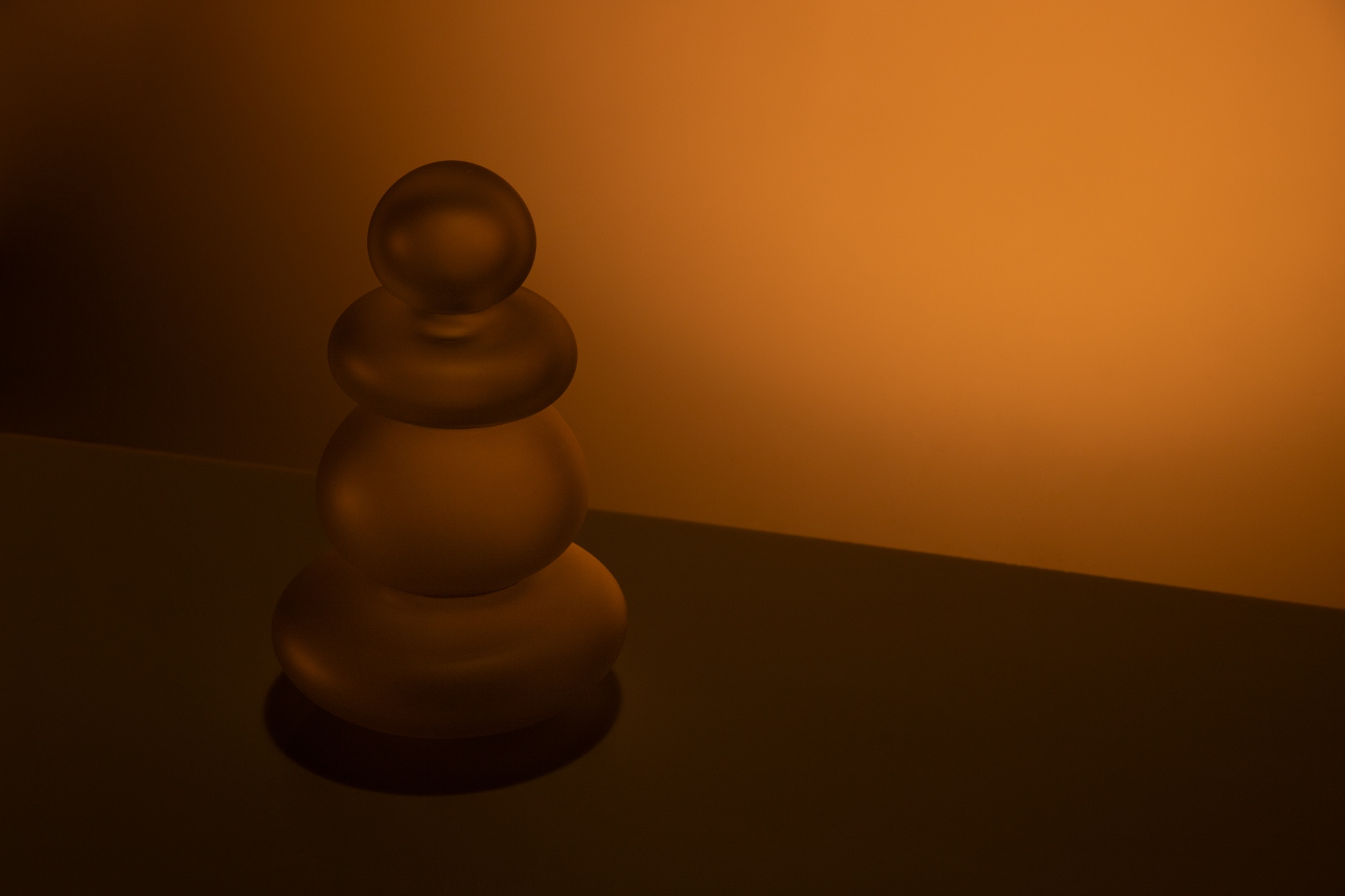 Lampe de table en verre soufflé transparent artisanale sur un fond ambre, éteinte, vue de côté.